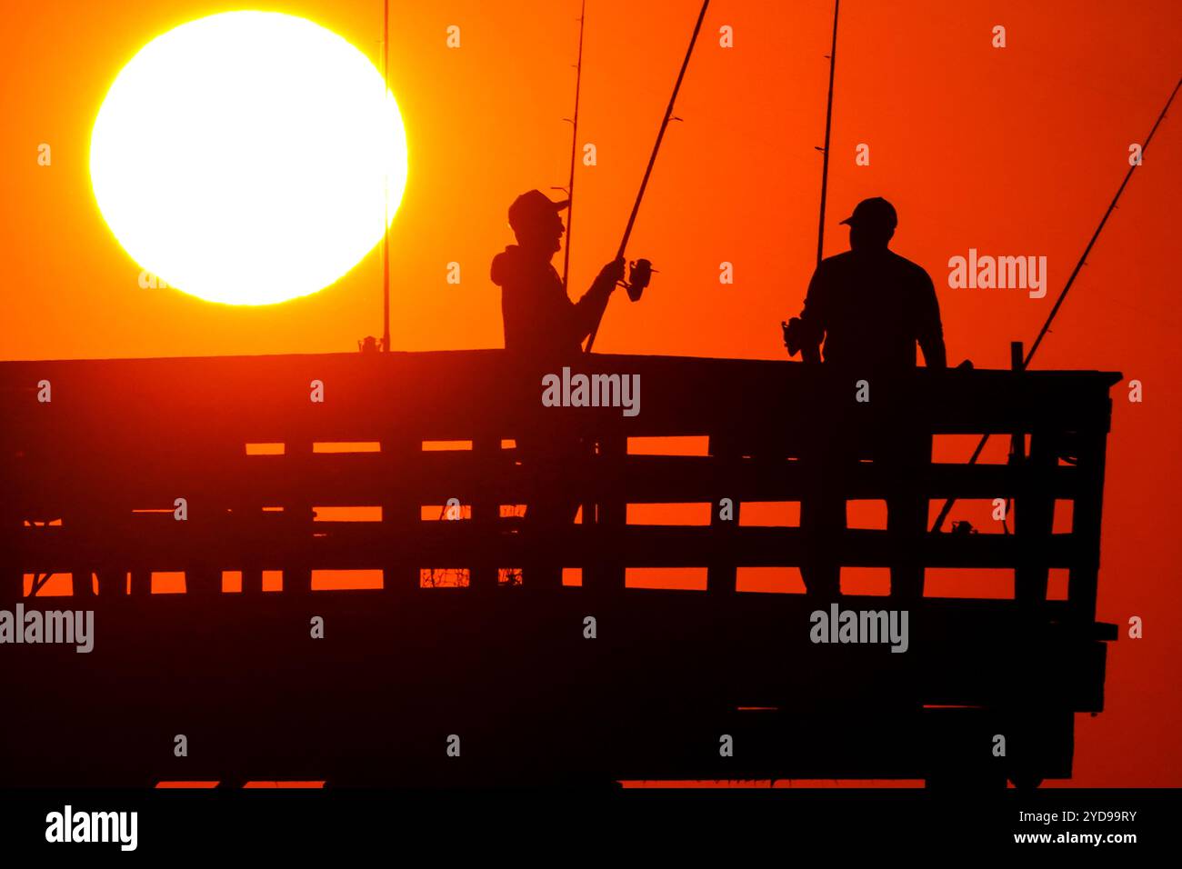 Isle Of Palms, Usa. Oktober 2024. Sportfischer, die vom Sonnenaufgang umrahmt werden, werfen ihre Linien, während die riesige orangene Sonne über dem Atlantischen Ozean vom Isle of Palms Pier am Front Beach am 25. Oktober 2024 in Isle of Palms, South Carolina, aufgeht. Sonniges und warmes Wetter wird für die nächsten Wochen vorhergesagt. Quelle: Richard Ellis/Richard Ellis/Alamy Live News Stockfoto