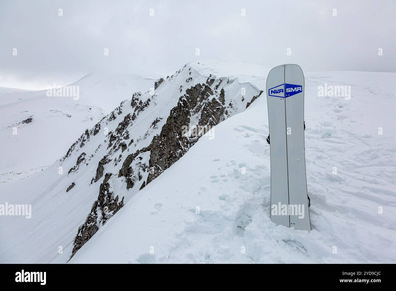 März 2024. Karpaten, Ukraine - Never Summer Splitboard auf einem schneebedeckten Gipfel mit Blick auf einen steilen, felsigen Berg wartet auf seinen Fahrer, bereit für die Fahrt Stockfoto