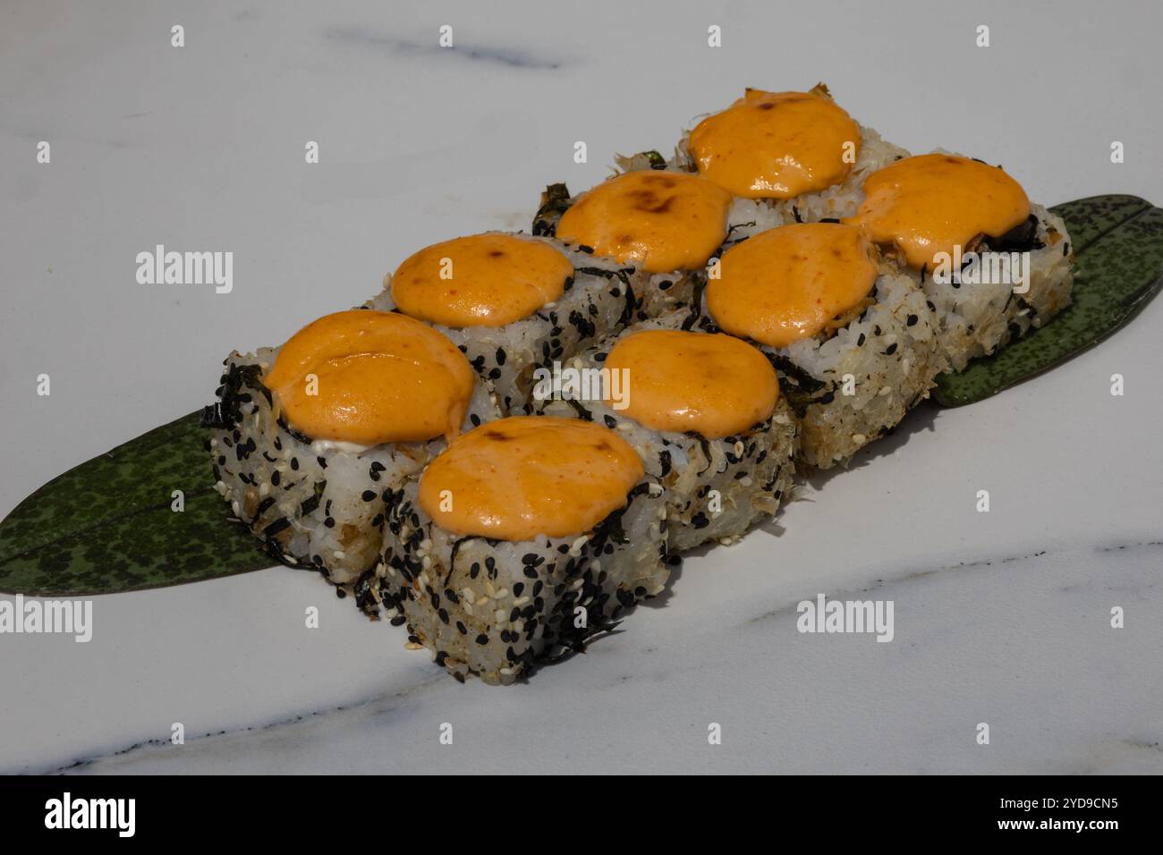 Nahaufnahme von Sushi-Brötchen mit würzigem Mayo-Belag auf grünem Blatt, serviert auf weißem Teller. Japanische Küche, traditionelle Küche und Gourmetrestaurant Stockfoto