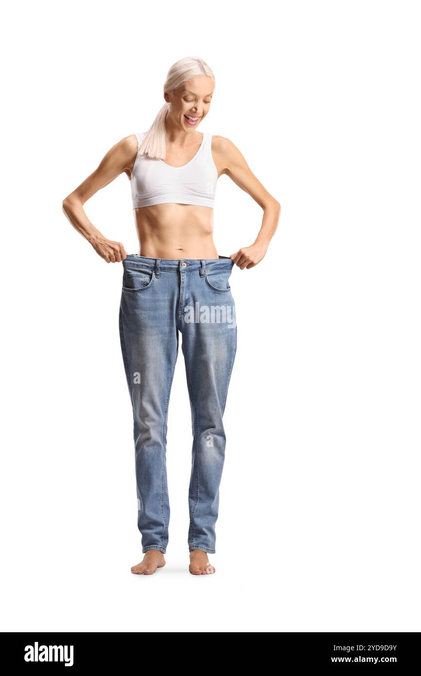 Glückliche schlanke Frau, die eine alte Jeans auf weißem Hintergrund anprobiert Stockfoto