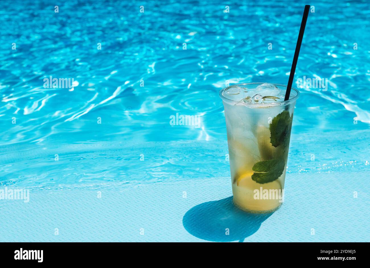 Köstliches Eisgetränk mit Limette, Zitrone und Minze auf der Seite des Pools. Leckerer frischer Mojito auf dem Hintergrund von klarem blauem Wasser. Stockfoto