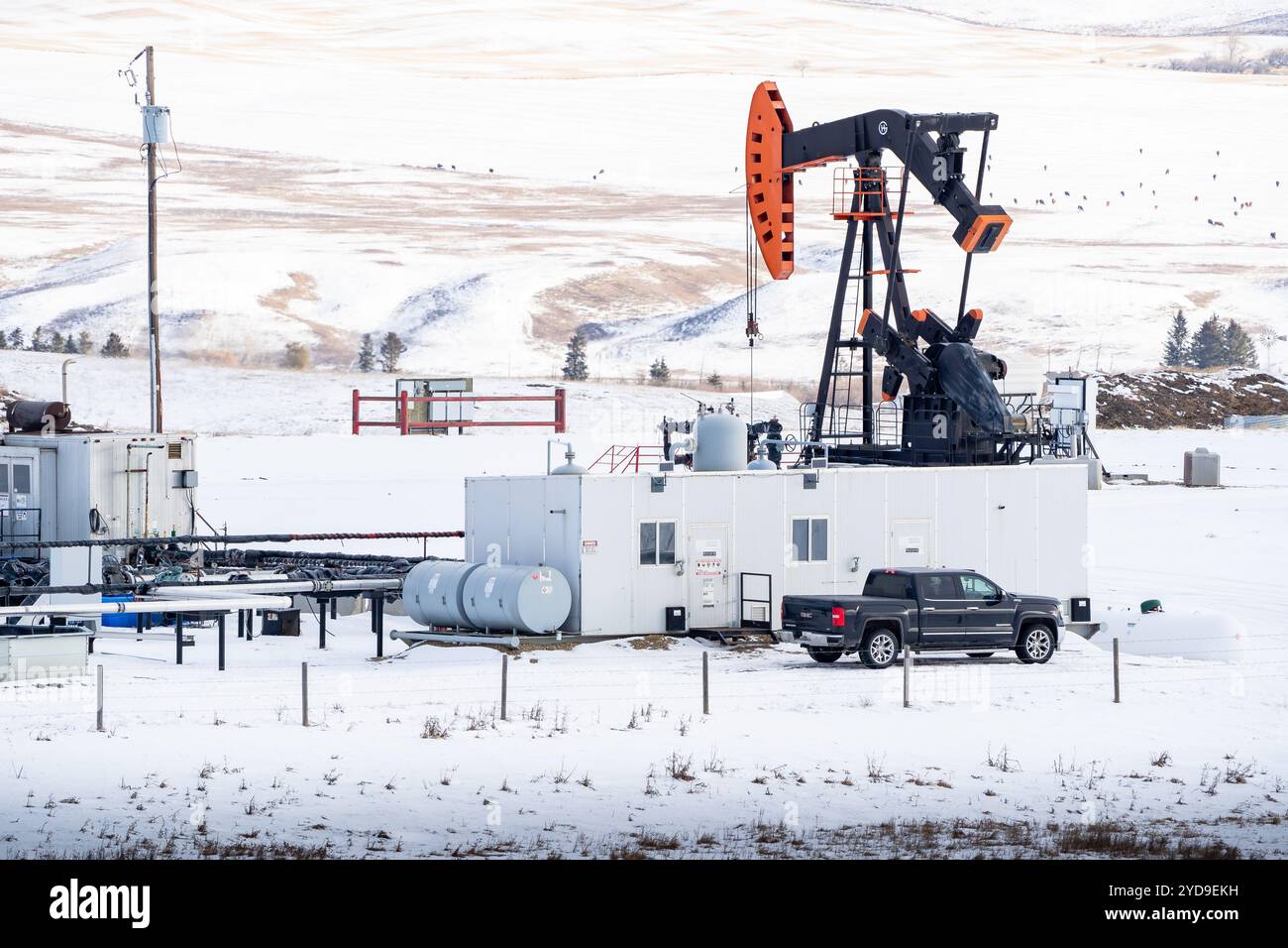 Rocky View County Alberta Canada, 20. Januar 2024: Arbeiter an einer Ölbohrstelle im Winter mit Blick auf einen Pumpenheber mit Gebäuden und entferntem sn Stockfoto