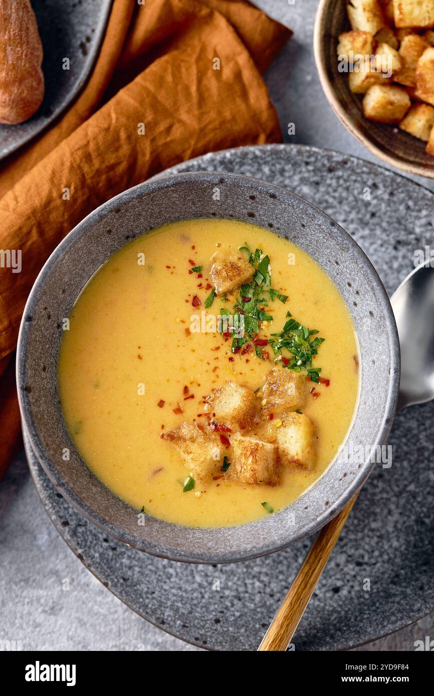 Schüssel Kartoffelpüree mit einem Löffel auf dem Teller. Die Schüssel wird mit gelbem Suppenpüree gefüllt und mit Croutons und Parseln belegt Stockfoto