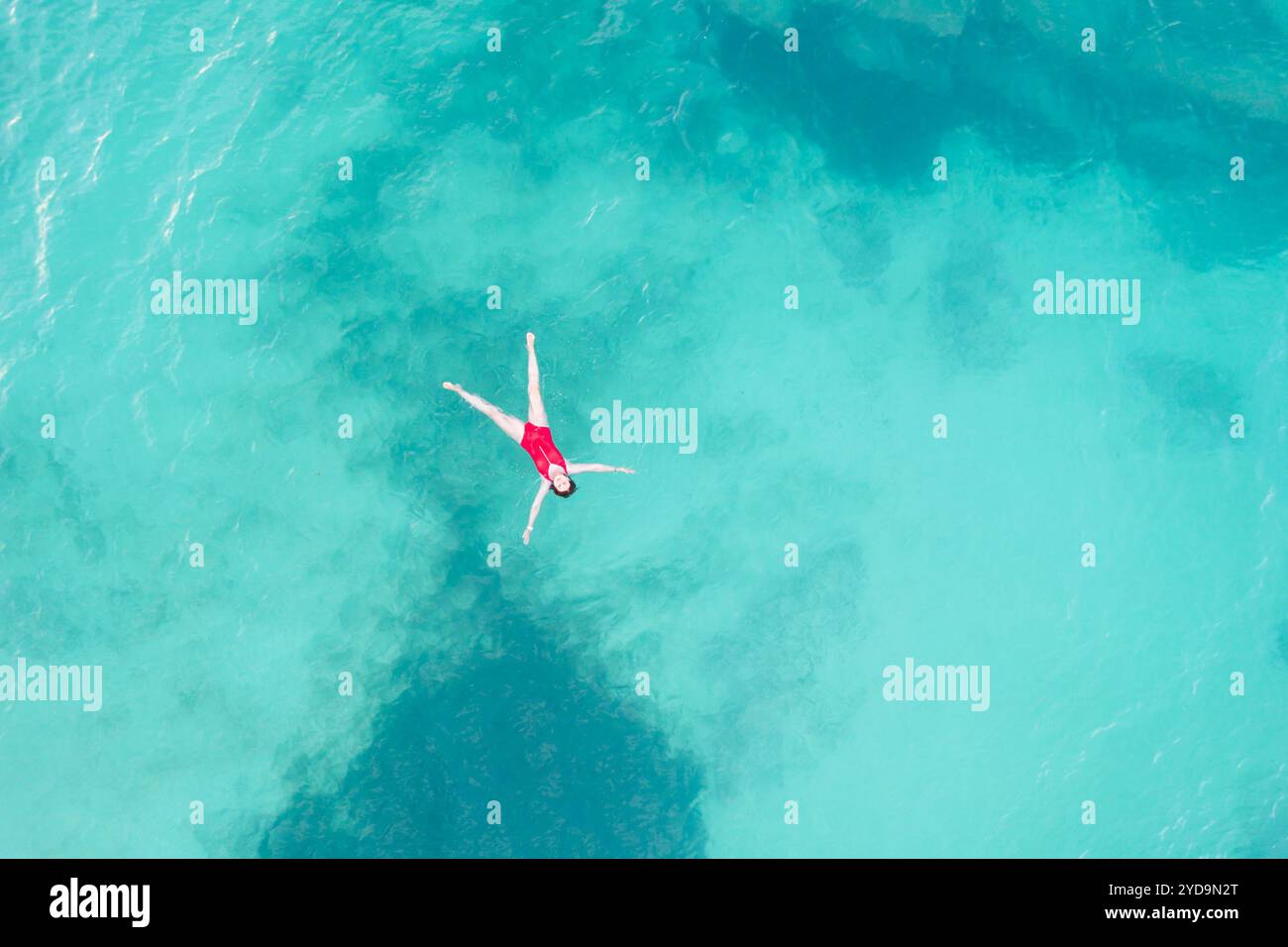 Aus der Luft eine Frau mit rotem Badeanzug, die auf einer transparenten türkisfarbenen Wasseroberfläche am karibischen Strand liegt. Reisen und Urlaub Stockfoto