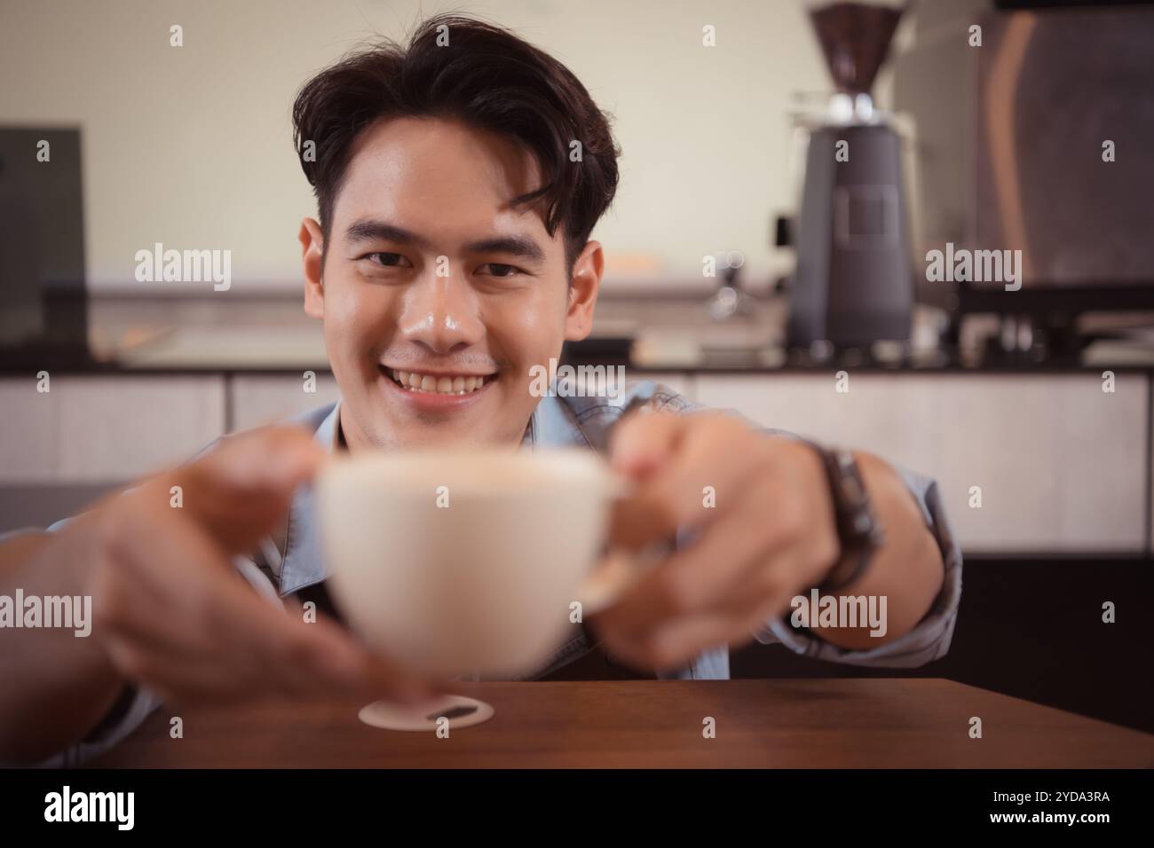 Dieser junge Barista, der einen Latte Kaffee zubereiten möchte, um die Gäste sowohl in Aussehen als auch im Geschmack zufriedenzustellen, ist diese Tasse Kaffee Stockfoto