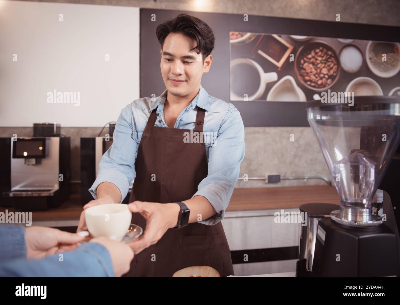 Dieser junge Barista, der einen Latte Kaffee zubereiten möchte, um die Gäste sowohl in Aussehen als auch im Geschmack zufriedenzustellen, ist diese Tasse Kaffee Stockfoto