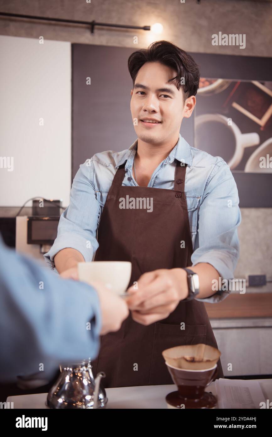 Dieser junge Barista, der einen Latte Kaffee zubereiten möchte, um die Gäste sowohl in Aussehen als auch im Geschmack zufriedenzustellen, ist diese Tasse Kaffee Stockfoto