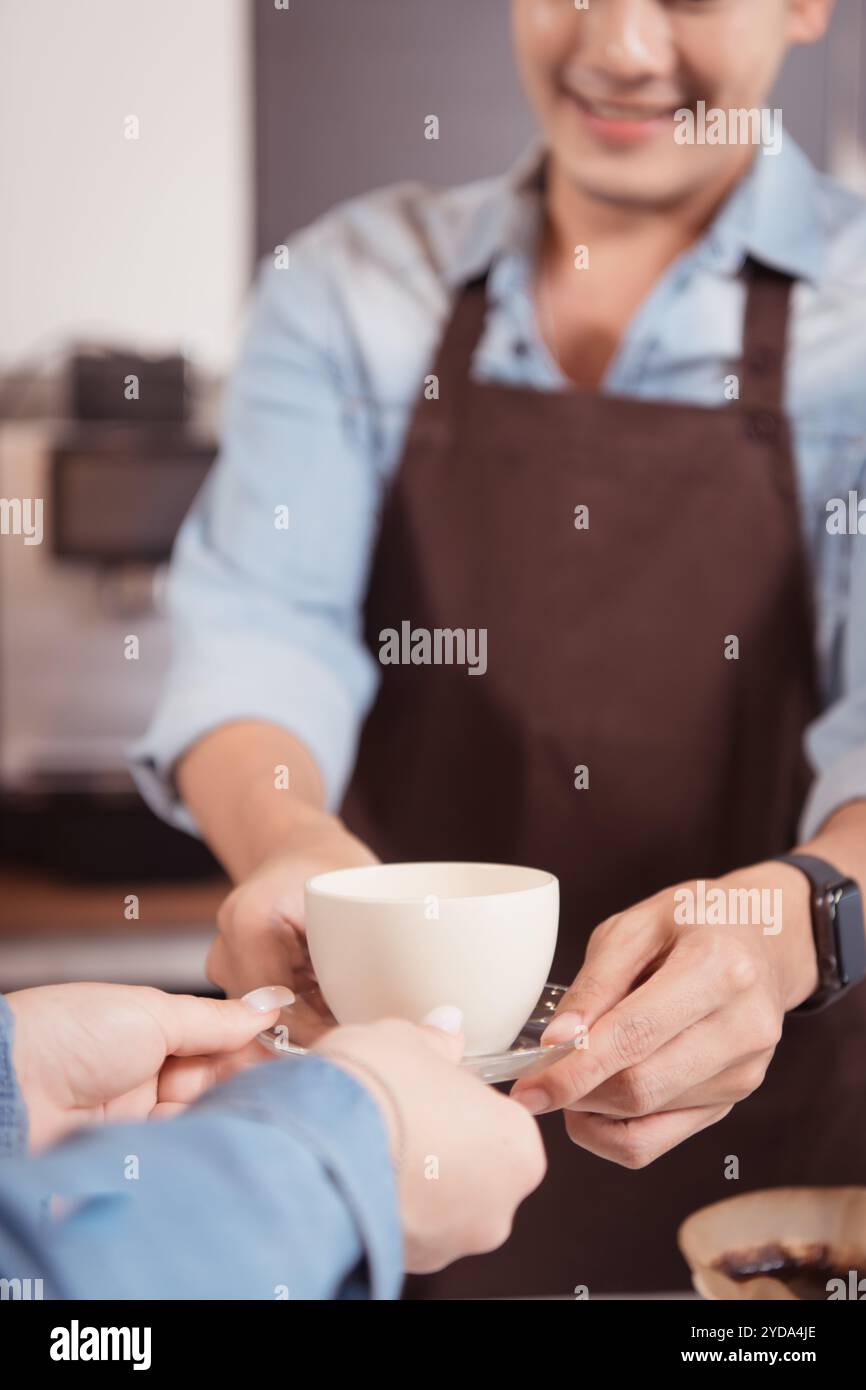 Dieser junge Barista, der einen Latte Kaffee zubereiten möchte, um die Gäste sowohl in Aussehen als auch im Geschmack zufriedenzustellen, ist diese Tasse Kaffee Stockfoto