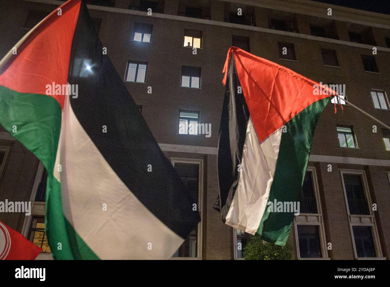 Rom, Italien. Oktober 2024. Demonstranten schwenken palästinensische Flaggen, während jemand oben während der Demonstration aus dem Fenster schaut, als Reaktion auf den internationalen Aufruf #StopBotschaften am "Freitag der Wut" für Gaza, gegen den anhaltenden Völkermord im nördlichen Gazastreifen zu protestieren und die Waffenlieferungen an Israel zu stoppen, der von der palästinensischen Studentenbewegung in der Nähe der US-Botschaft in Rom organisiert wird. Auf der ganzen Welt haben zahlreiche Proteste stattgefunden, um auf den Aufruf der Hamas-Bewegung zu reagieren, die die arabischen und islamischen Massen und die freien Menschen der Welt dazu einlud, aktiv˜ Stockfoto