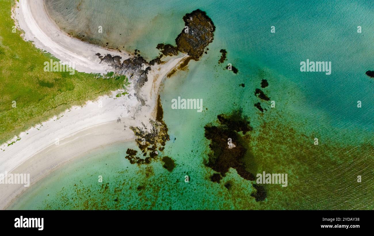 Ein Blick aus der Vogelperspektive auf einen unberührten Strand, der sich um einen Felsvorsprung schlängelt, wo türkisfarbenes Wasser auf grünes Gras und weißen Sand trifft. Kolbeinsanden Beach, Stockfoto