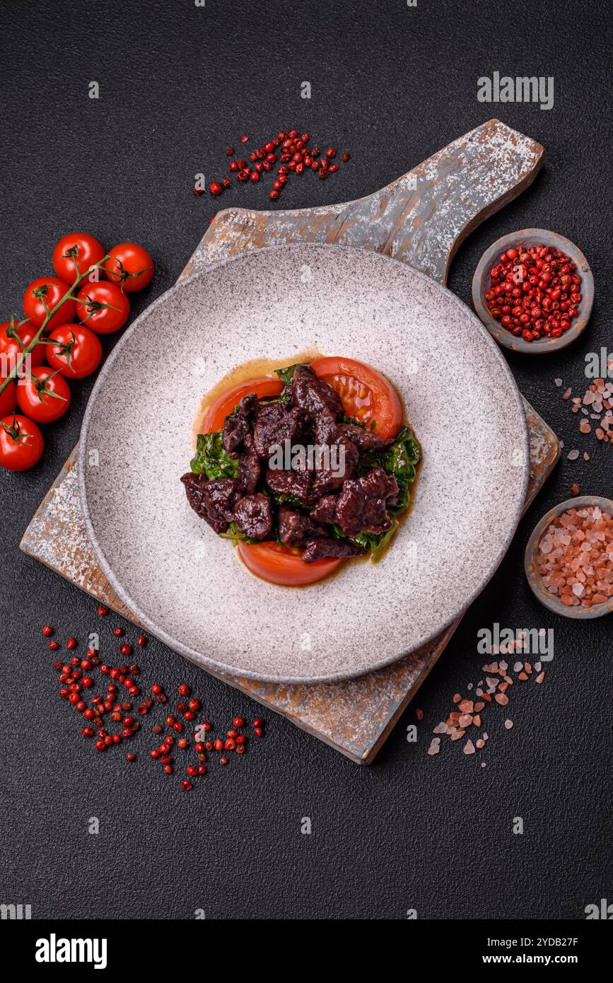 Köstlicher warmer Salat aus Hühnerleber, Spinat, Rucola, Tomaten mit Salz, Gewürzen und Kräutern auf dunklem Betonhintergrund Stockfoto