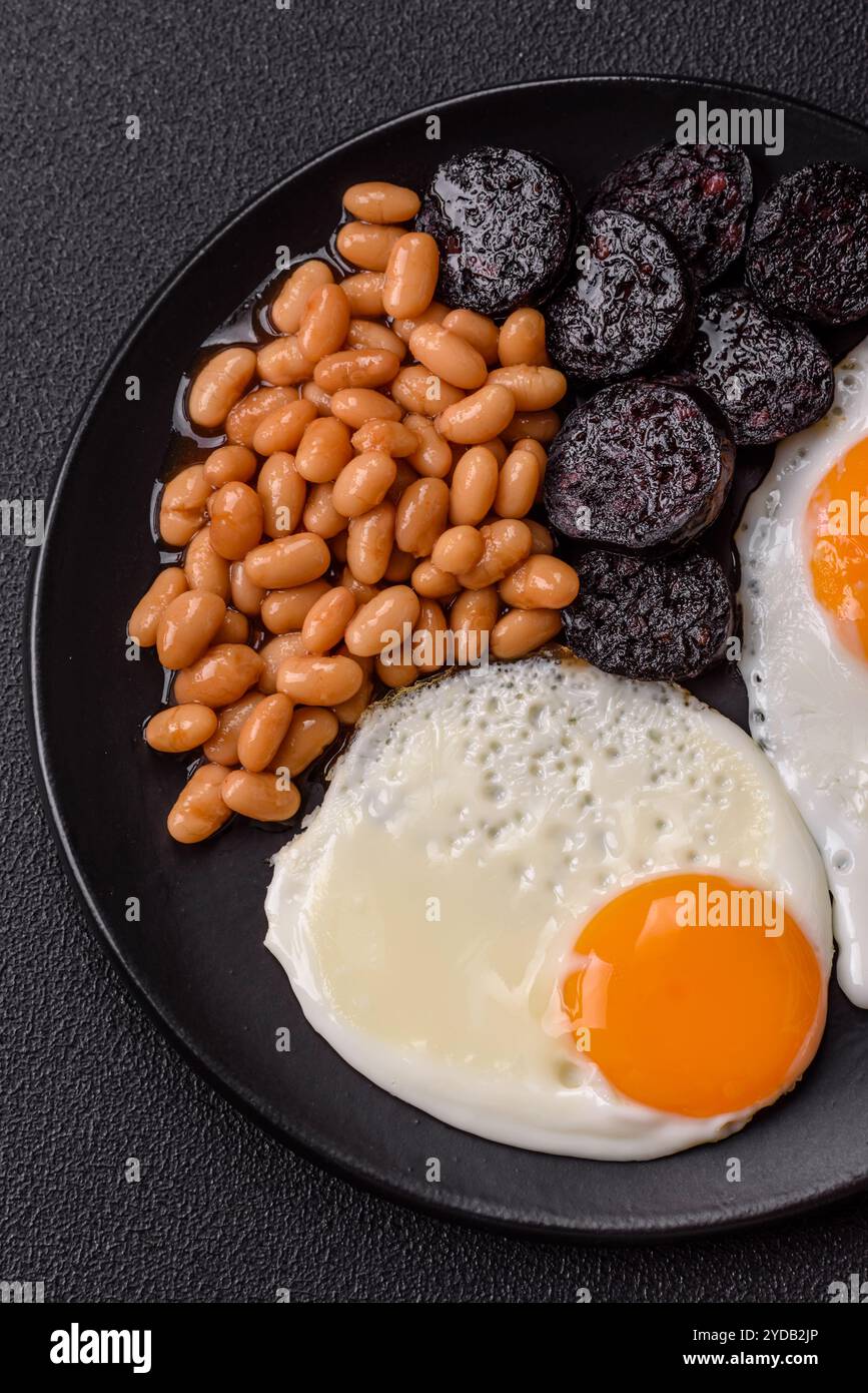 Englisches Frühstück mit Spiegeleiern, Speck, Bohnen, Tomaten, Gewürzen und Kräutern Stockfoto