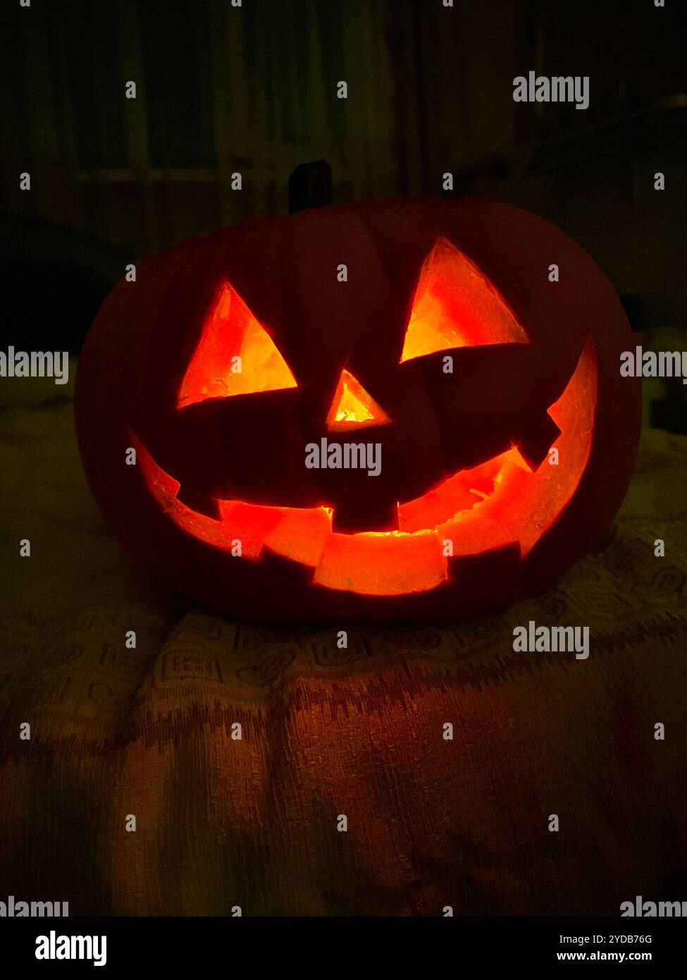 Gruseliger Halloween-Kürbis mit geschnitztem Gesicht, das im Dunkeln leuchtet - Smartphone-aufgenommenes Stockfoto