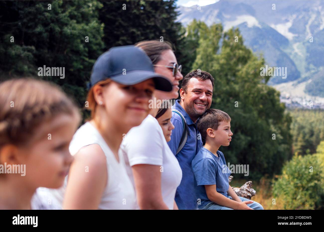 Glückliche Familie von Touristen sitzt auf Baumstämmen und genießt die Berglandschaft. Rückansicht Stockfoto