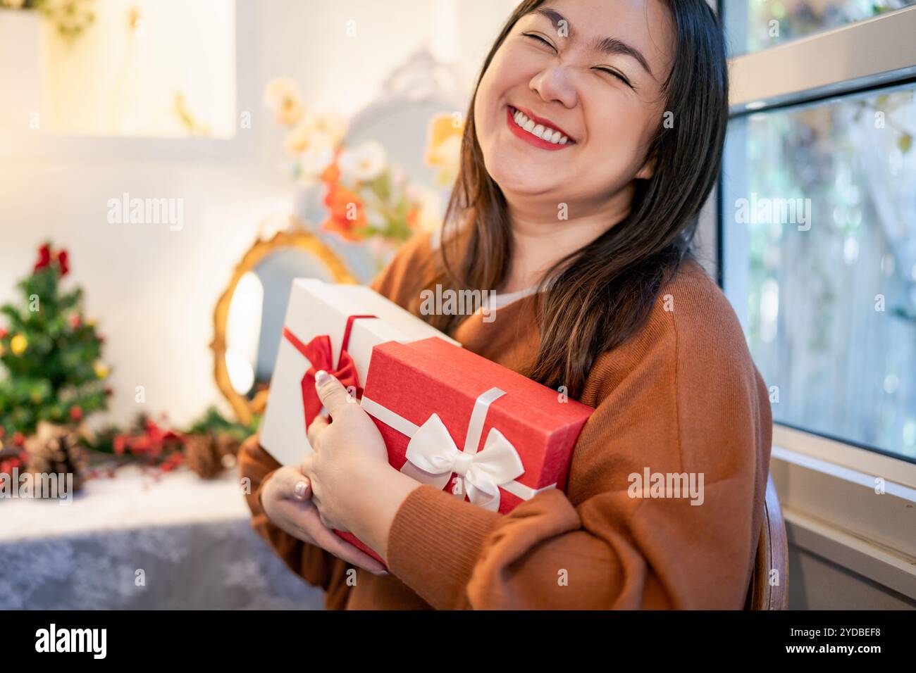 Glückliche asiatische Frau, die Geschenkbox umarmt. Empfang eines Weihnachtsgeschenks. Fröhliches Mädchen mit Weihnachtsgeschenk oder offenem Weihnachtsgeschenk boxÂ Neujahrsgeburt Stockfoto