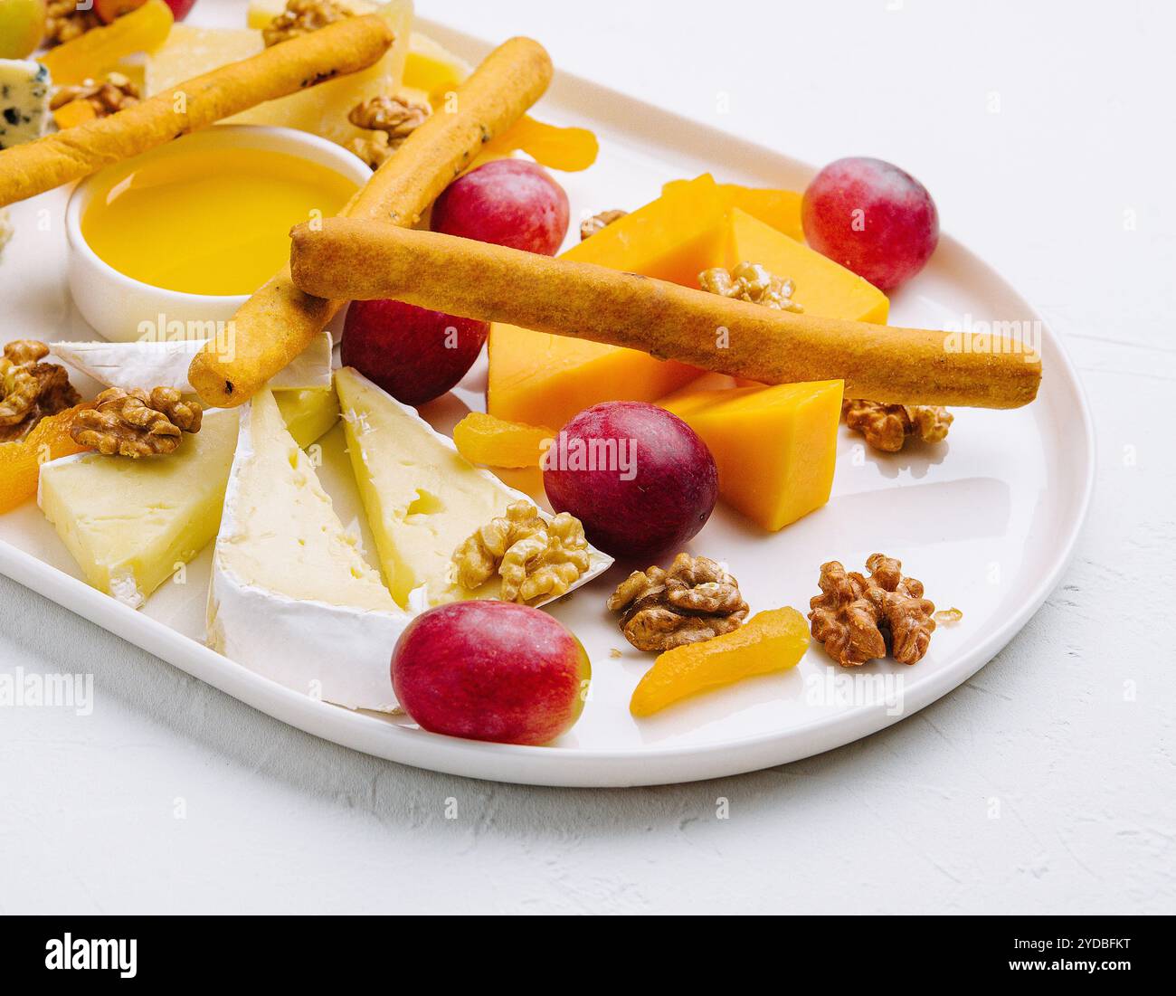 Käseplatte mit Honig, Nüssen und roten Trauben Stockfoto