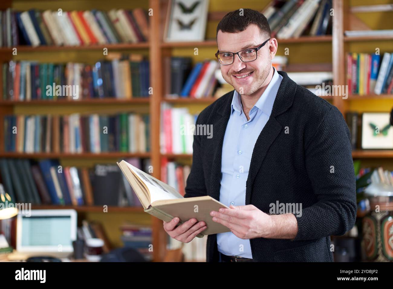 Mann liest Buch in der Hochschulbibliothek viele Bücher auf einem Hintergrund Stockfoto