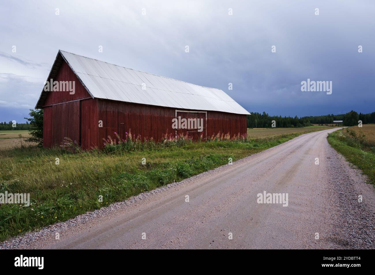 Rote Scheune neben einer Schotterstraße in einer ländlichen Landschaft in Finnland Stockfoto