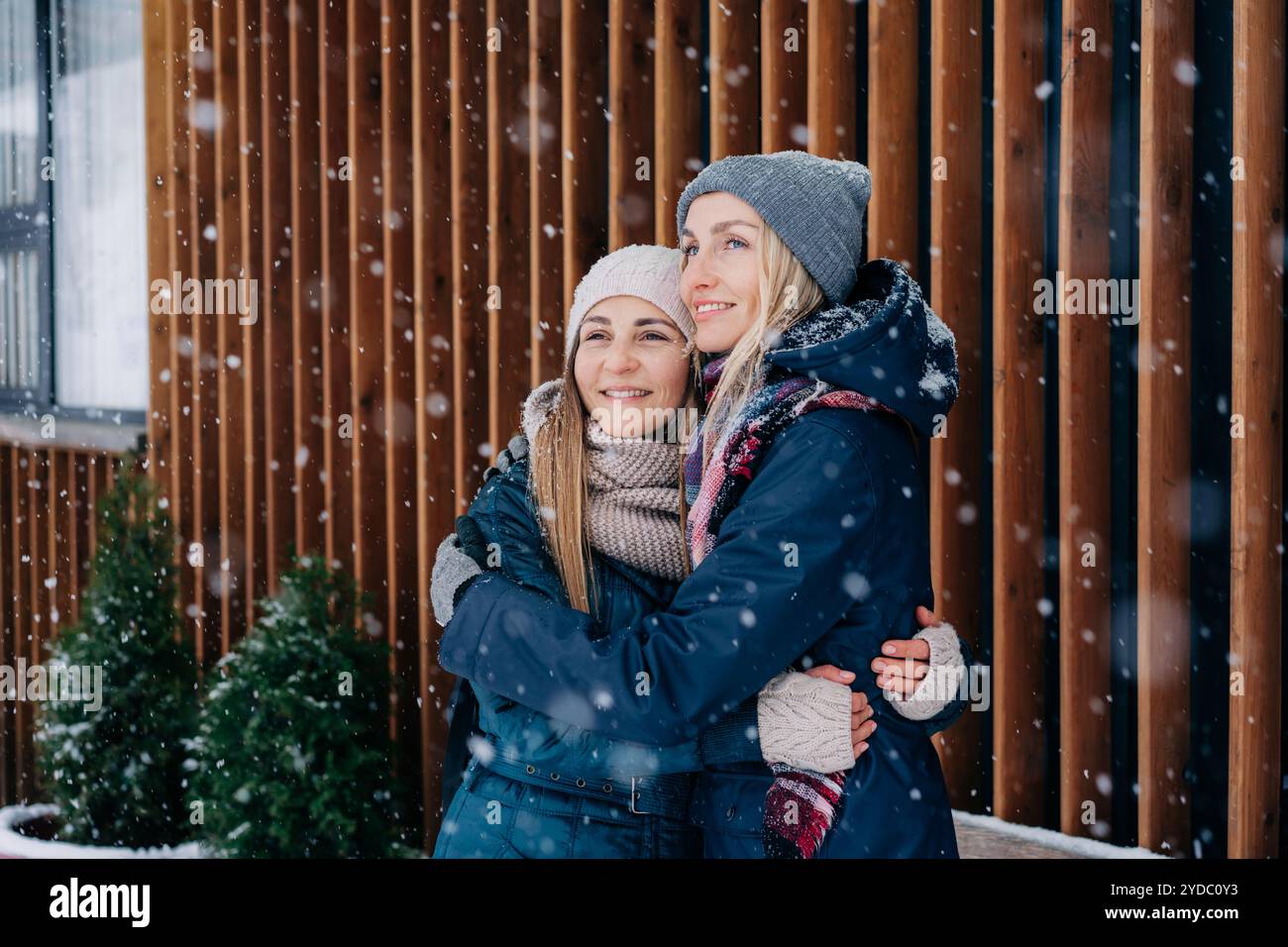 Zwei Freundinnen, die stehen und kuscheln, freuen sich über das verschneite Wetter. Stockfoto