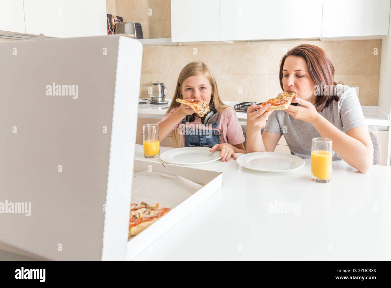 Mutter und Tochter in der Küche sitzen, essen Pizza und Spaß haben. Fokus auf Tochter Stockfoto
