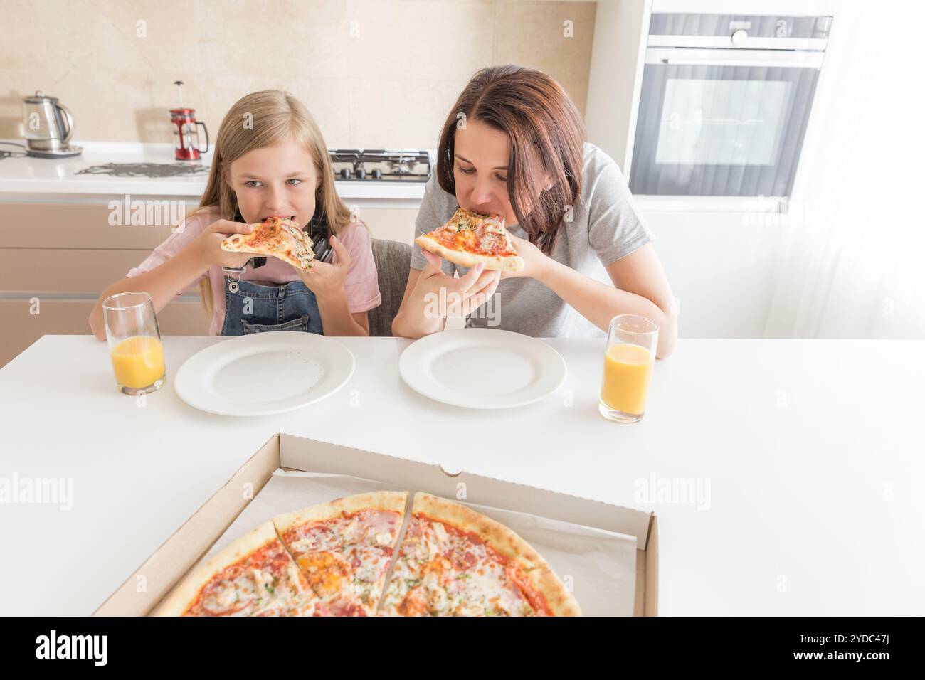 Mutter und Tochter in der Küche sitzen, essen Pizza und Spaß haben. Fokus auf Tochter Stockfoto