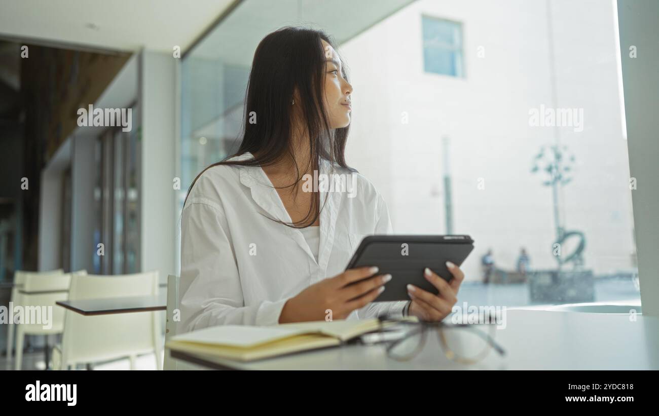 Frau, die in einem modernen Büro mit natürlichem Licht an einem Tablet arbeitet und eine professionelle und dynamische Umgebung bietet. Stockfoto