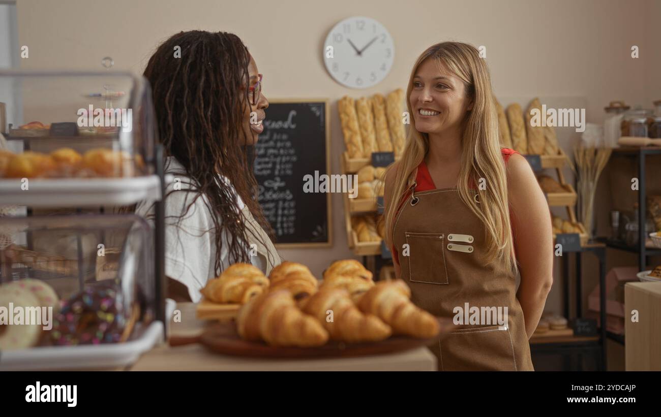 Frauen sprechen in der Bäckerei mit Brot und Gebäck, umgeben von Regalen und Tafel-Menü im Hintergrund Stockfoto