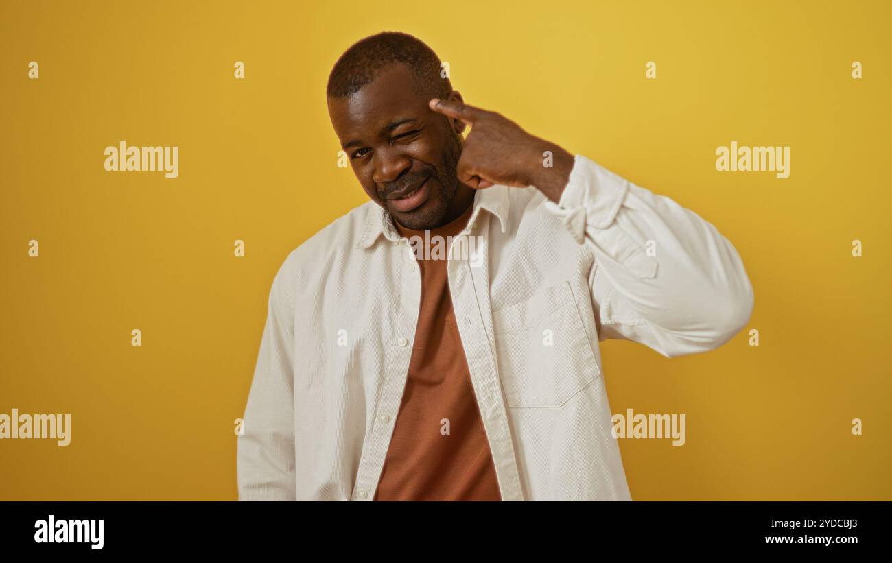 Ein junger afroamerikanischer Mann gibt spielerisch Gesten vor einem lebhaften gelben Hintergrund und hebt eine selbstbewusste und attraktive Persönlichkeit hervor. Stockfoto