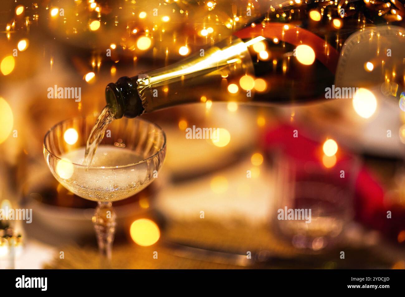 Champagner wird aus der Flasche in ein stilvolles Glas gegossen. Glitzernde goldene Festlichter vor Hintergrund. Blasen steigen in Sekt auf. Nahaufnahme von PR Stockfoto