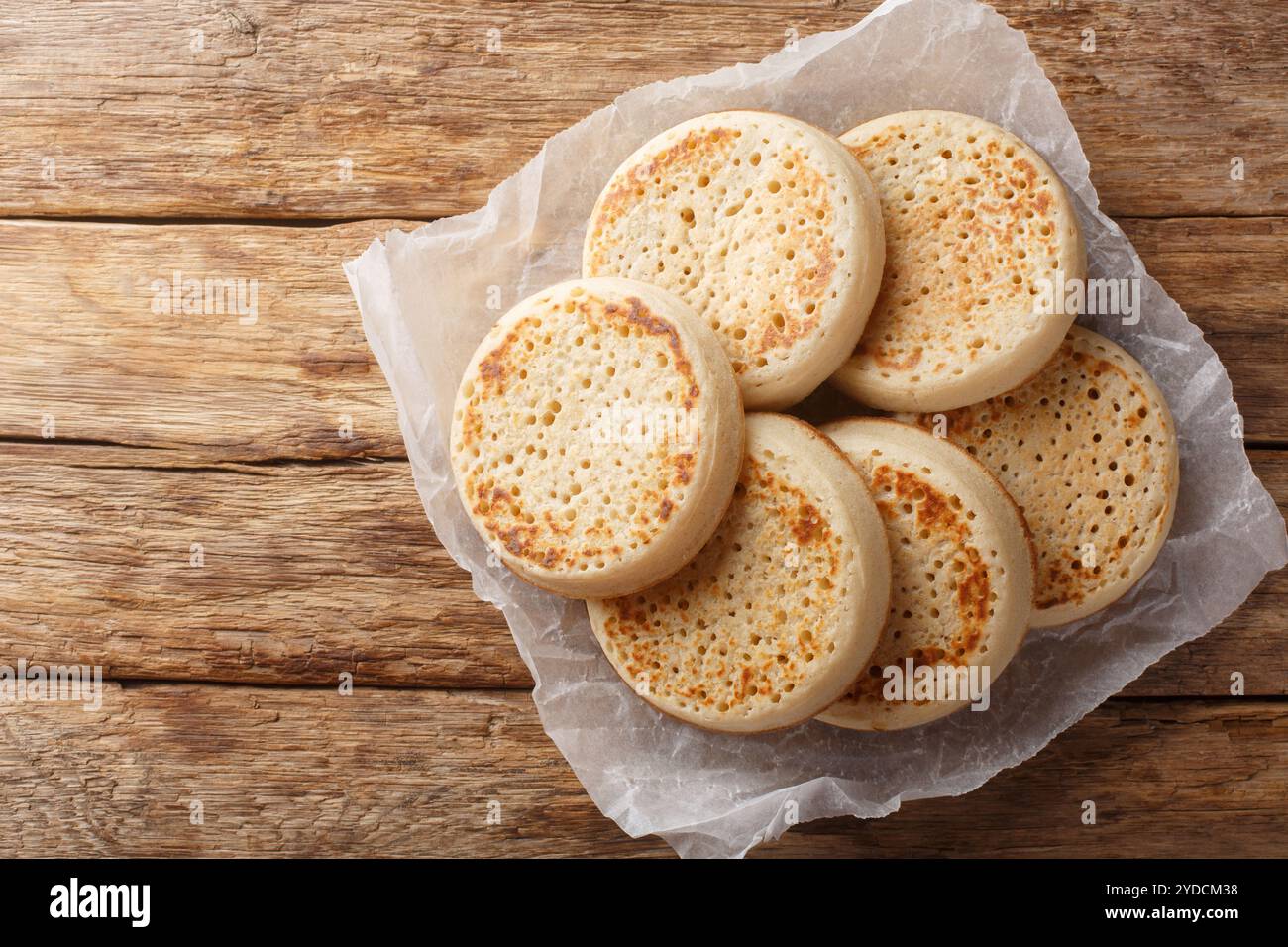Frisch aus dem Ofen englische Crumpets oder poröses Brot in Nahaufnahme auf Pergament auf einem alten Tisch. Horizontale Draufsicht von oben Stockfoto