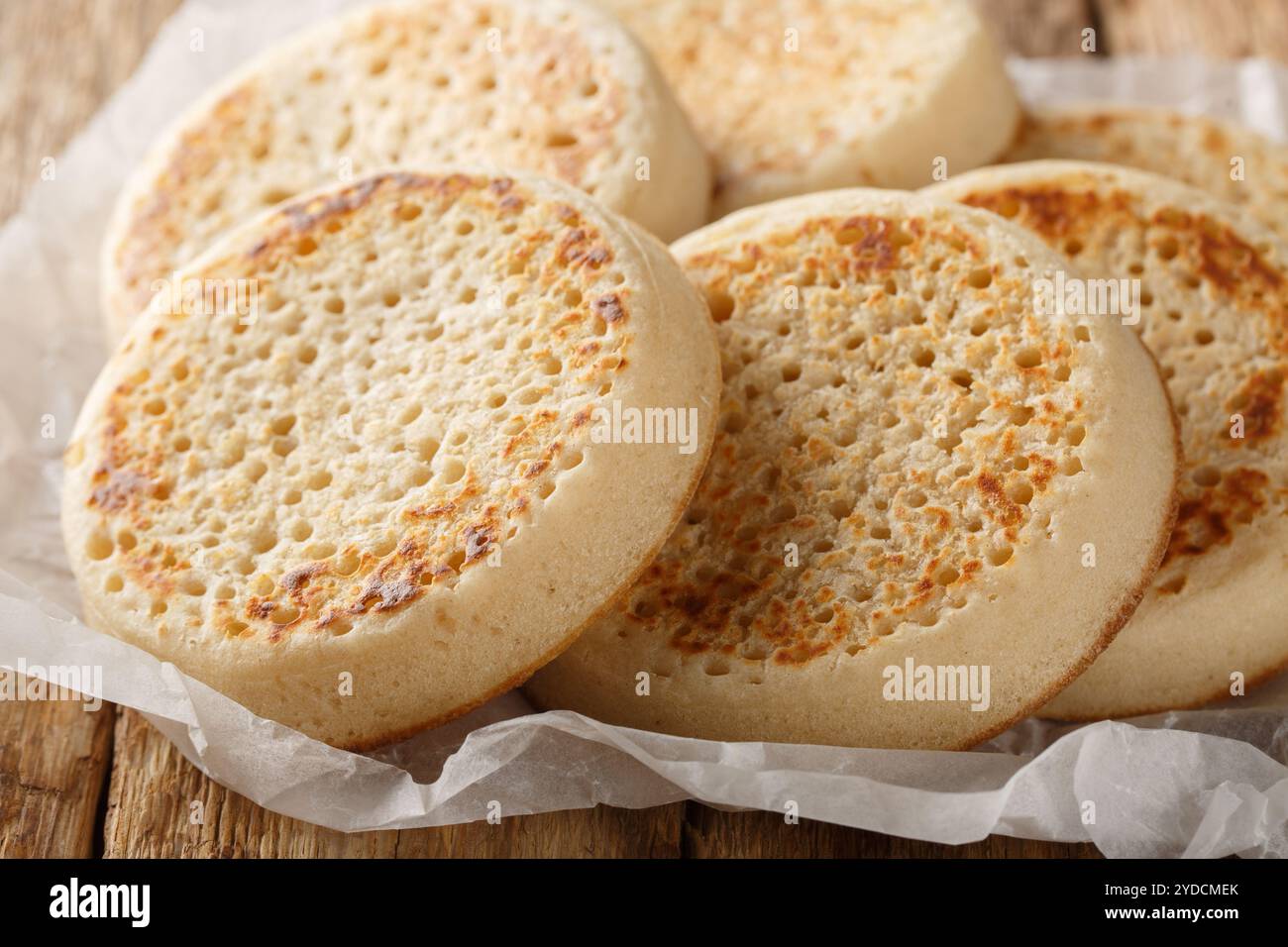 Frisch aus dem Ofen englische Crumpets oder poröses Brot in Nahaufnahme auf Pergament auf einem alten Tisch. Horizontal Stockfoto