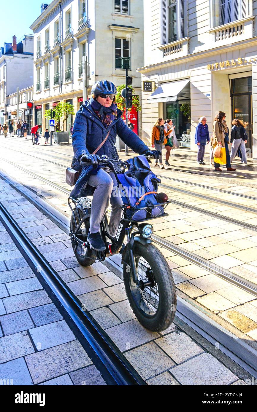Käuferin, die ein elektrisches Fahrrad neben der Straßenbahn auf einer nicht mit Fahrzeugen ausgestatteten Straße im Stadtzentrum fährt - Tours, Indre-et-Loire (37), Frankreich. Stockfoto