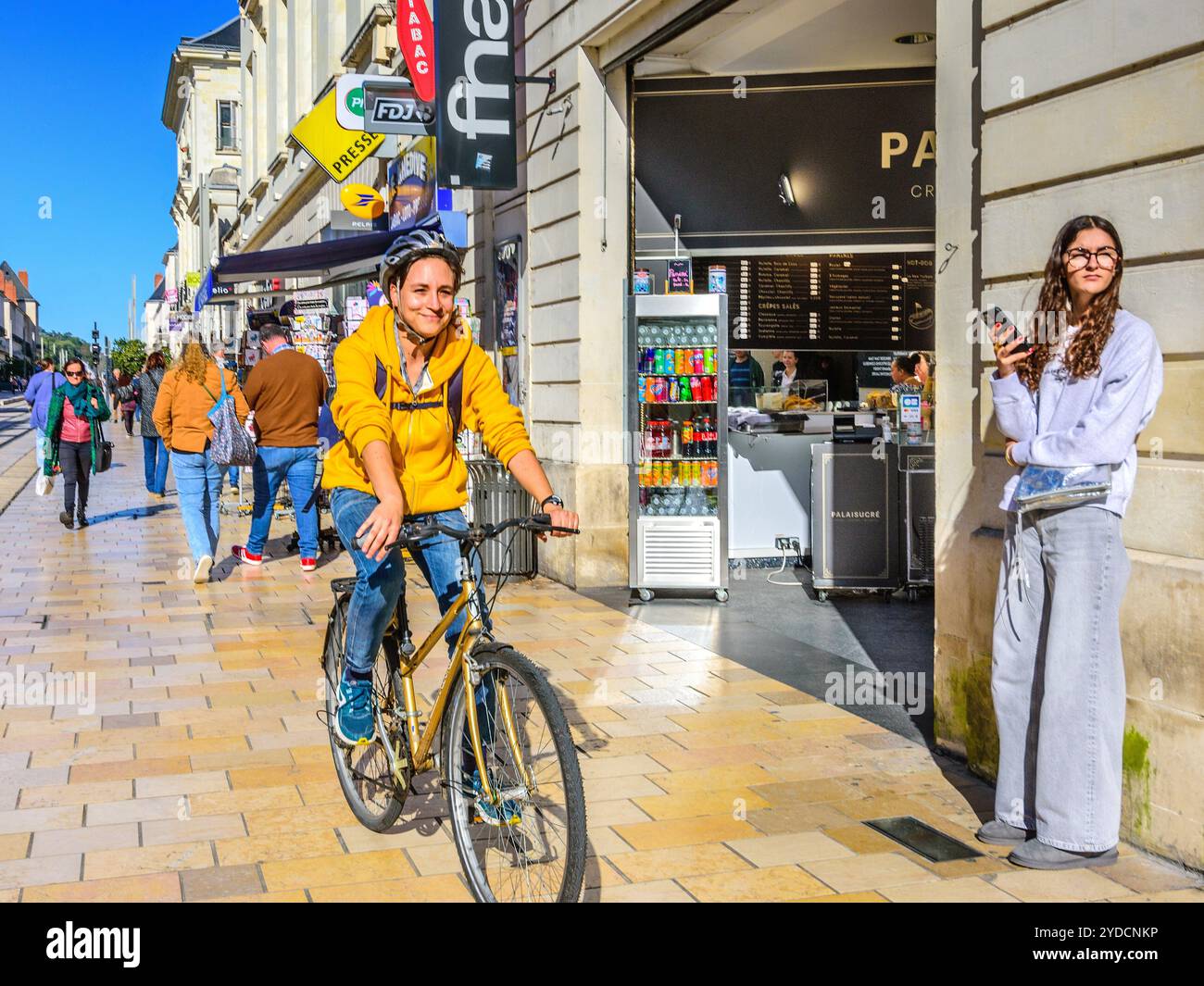 Frau, die mit dem Fahrrad neben der Straßenbahn auf der nicht mit dem Fahrzeug befahrenen Straße im Stadtzentrum unterwegs ist - Tours, Indre-et-Loire (37), Frankreich. Stockfoto
