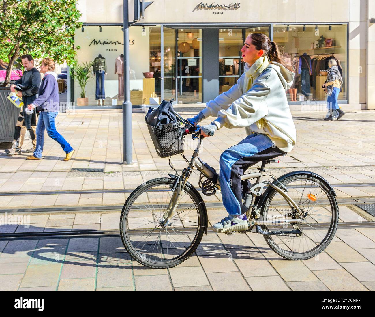 Frau, die mit dem Fahrrad neben der Straßenbahn auf der nicht mit dem Fahrzeug befahrenen Straße im Stadtzentrum unterwegs ist - Tours, Indre-et-Loire (37), Frankreich. Stockfoto