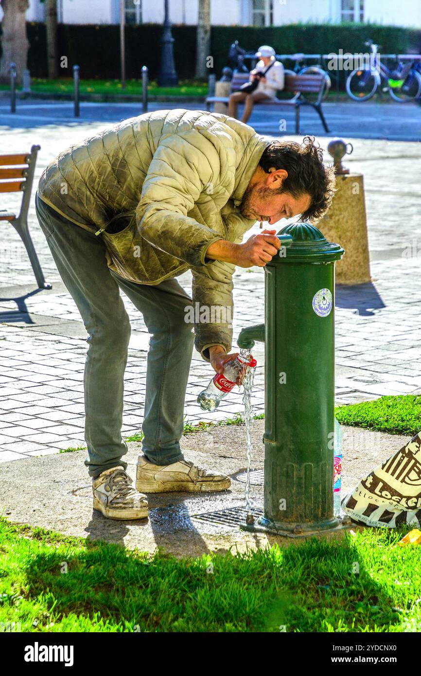 Arbeitsloser und unbewohnter Vagrant, der Wasser aus öffentlichen Wasserhähnen in Plastikflaschen gießt - Tours, Indre-et-Loire (37), Frankreich. Stockfoto