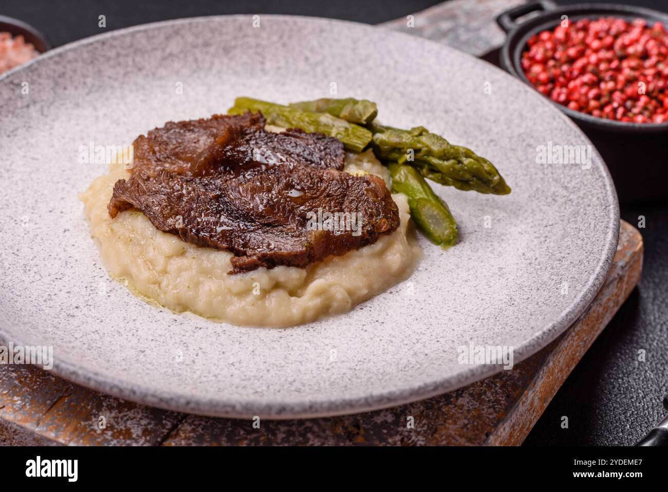 Saftiges Rindfleisch oder Schweinefleisch in Scheiben geschnitten mit gekochtem Spargel, Salz und Gewürzen auf dunklem Betonhintergrund Stockfoto