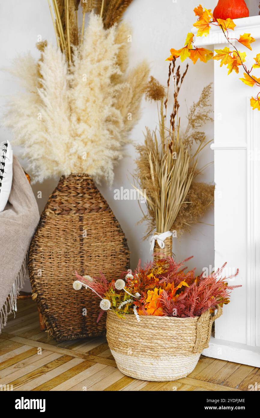 Getrocknete Blumen und gelbe Herbstblätter in gewebten Körben auf weißem Wandhintergrund, Herbstdekor im ästhetischen Innenraum des Hauses. Stockfoto