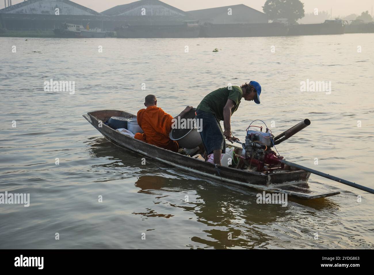 Thailand. Oktober 2024. Ein Mönch sitzt bei Sonnenaufgang auf einem Boot, während er seinen Opferkorb vorbereitet, und sein Fahrer startet den Motor auf dem Chao Phraya River. Die Tradition, hundert Mönchen in Pathum Thani, Thailand, Almosen zu geben, ist eine jahrhundertealte buddhistische Zeremonie, die entlang von Flüssen und Kanälen nach dem Ende der buddhistischen Fastenzeit stattfindet. Mönche versammeln sich in Booten, um Opfer von Einheimischen zu erhalten, die Essen zubereiten und an der Verdienste teilnehmen. Diese Veranstaltung feiert Gemeinschaft, Glauben und kulturelles Erbe. Quelle: SOPA Images Limited/Alamy Live News Stockfoto