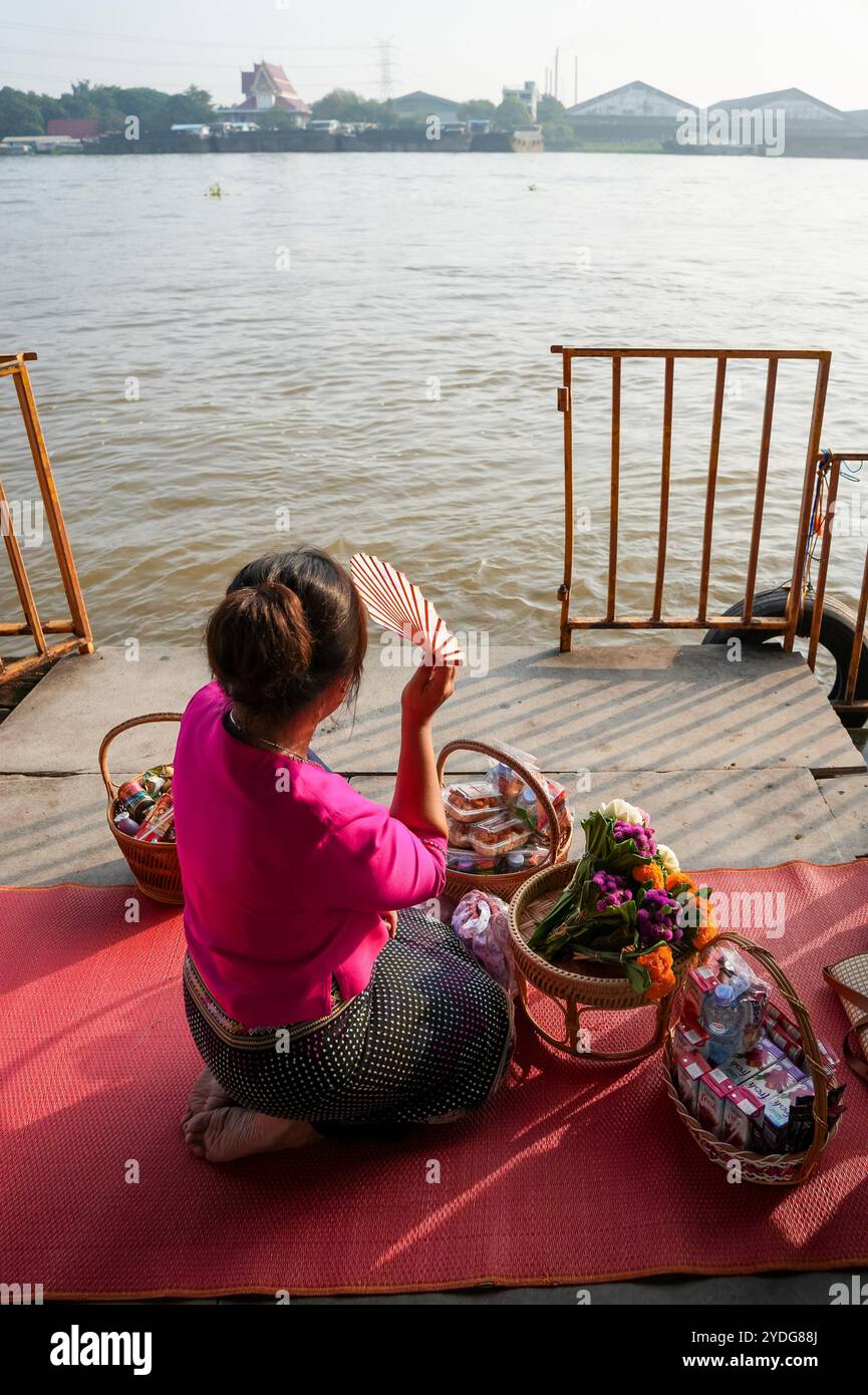 Thailand. Oktober 2024. Am Ufer des Chao Phraya am Wat Chin Wararam Worawihan Tempel in der Provinz Pathum Thani, Thailand, wird eine Thailändische Frau mit einem Fan gesehen, die Almosen an die Mönche überreicht. Die Tradition, hundert Mönchen in Pathum Thani, Thailand, Almosen zu geben, ist eine jahrhundertealte buddhistische Zeremonie, die entlang von Flüssen und Kanälen nach dem Ende der buddhistischen Fastenzeit stattfindet. Mönche versammeln sich in Booten, um Opfer von Einheimischen zu erhalten, die Essen zubereiten und an der Verdienste teilnehmen. Diese Veranstaltung feiert Gemeinschaft, Glauben und kulturelles Erbe. Quelle: SOPA Images Limited/Alamy Live News Stockfoto