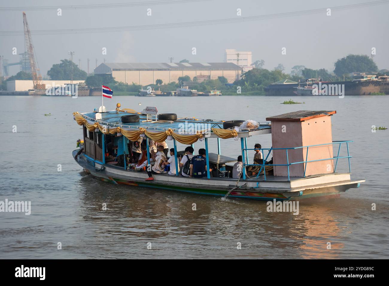 Ein Blick auf das Hauptboot mit der thailändischen Flagge, das Almosen von Menschen sammelt, die am Ufer des Chao Phraya am Wat Chin Wararam Worawihan Tempel in der Provinz Pathum Thani, Thailand, warten. Die Tradition, hundert Mönchen in Pathum Thani, Thailand, Almosen zu geben, ist eine jahrhundertealte buddhistische Zeremonie, die entlang von Flüssen und Kanälen nach dem Ende der buddhistischen Fastenzeit stattfindet. Mönche versammeln sich in Booten, um Opfer von Einheimischen zu erhalten, die Essen zubereiten und an der Verdienste teilnehmen. Diese Veranstaltung feiert Gemeinschaft, Glauben und kulturelles Erbe. Stockfoto