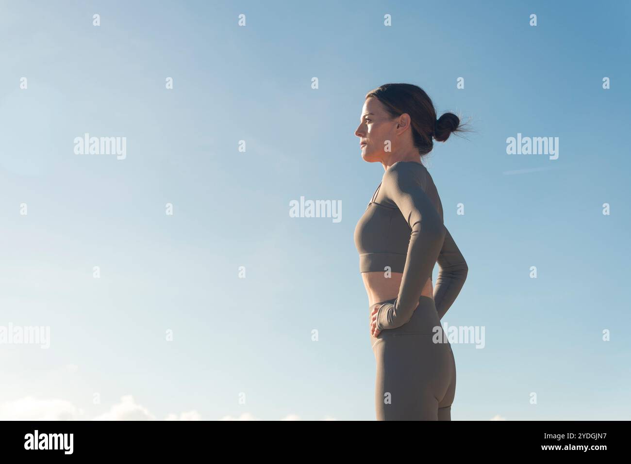 Sportliche Frau, die draußen in der Sonne steht und Hände auf Hüften hält Stockfoto