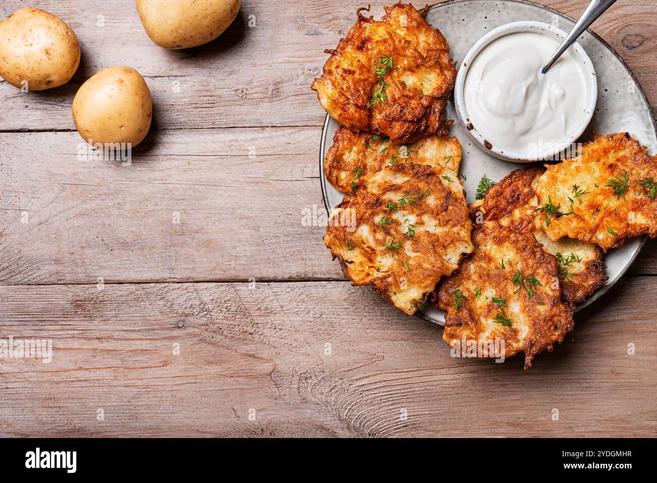 Kartoffellatkes mit Sauerrahm auf hölzernem Hintergrund, Draufsicht, Kopierraum. Traditionelle jüdische Latkes oder Levivot. Kartoffelrösti. Stockfoto