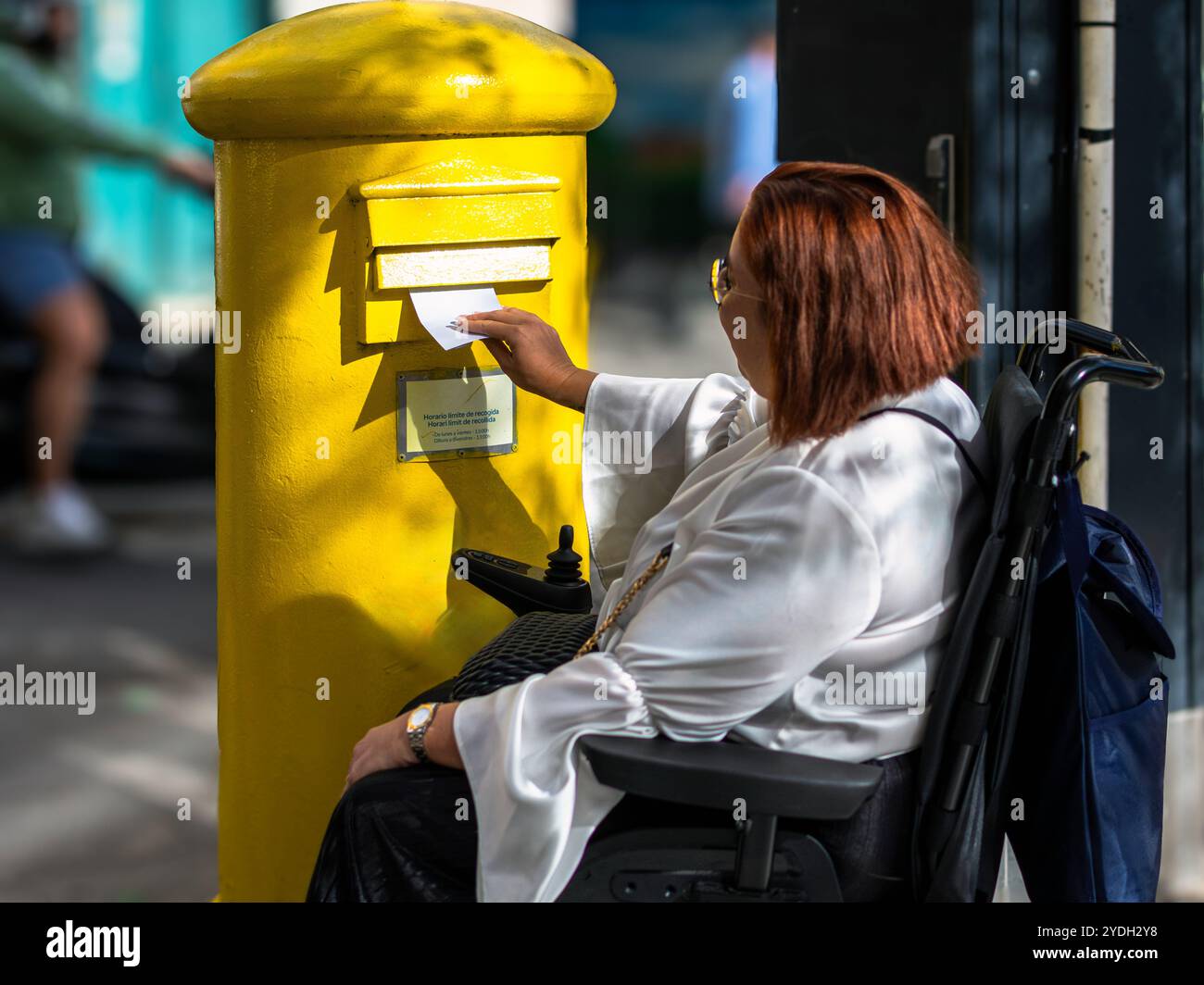 Frau im Rollstuhl postet einen Brief im gelben Briefkasten Stockfoto