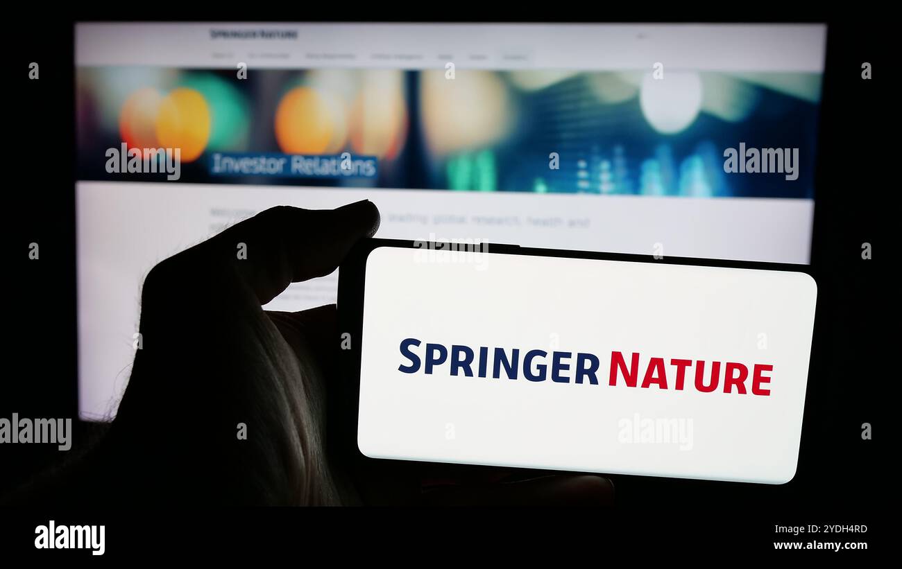 Person mit Smartphone und Logo des akademischen Verlags Springer Nature auf dem Bildschirm vor der Website. Schwerpunkt auf dem Display des Telefons. Stockfoto
