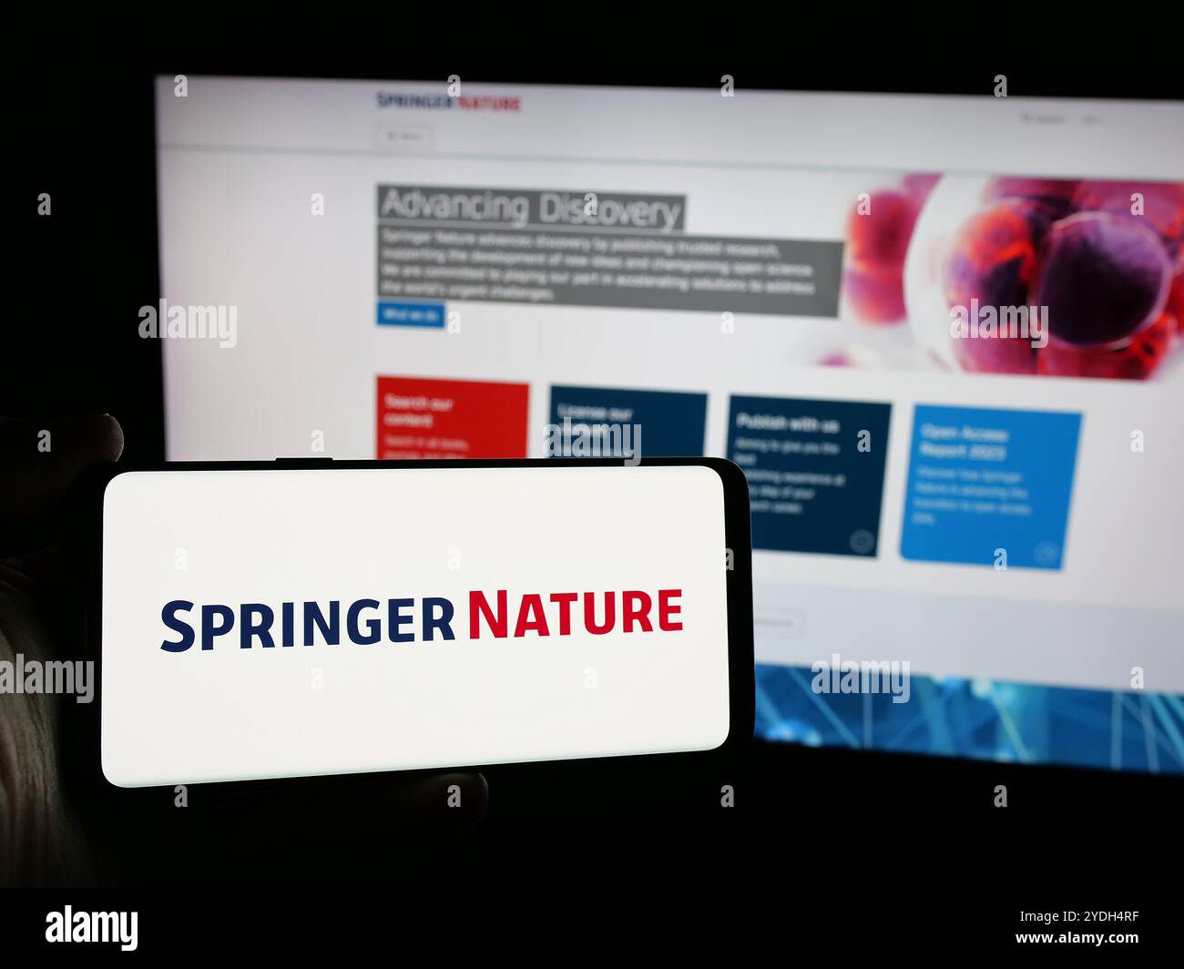 Person mit Mobiltelefon und Logo des akademischen Verlags Springer Nature auf dem Bildschirm vor der Webseite. Schwerpunkt auf dem Display des Telefons. Stockfoto