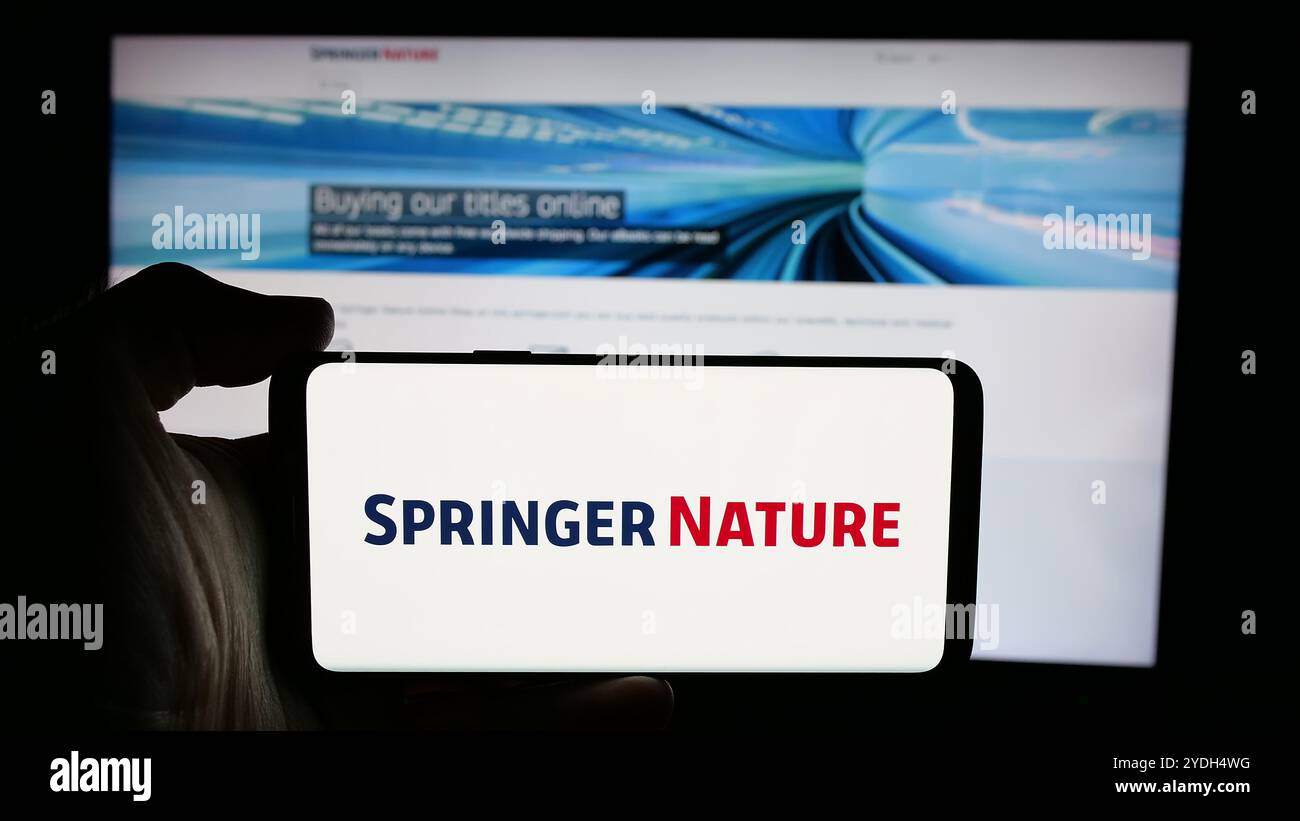 Person mit Handy und Logo des akademischen Verlags Springer Nature auf dem Bildschirm vor der Webseite des Unternehmens. Schwerpunkt auf dem Display des Telefons. Stockfoto