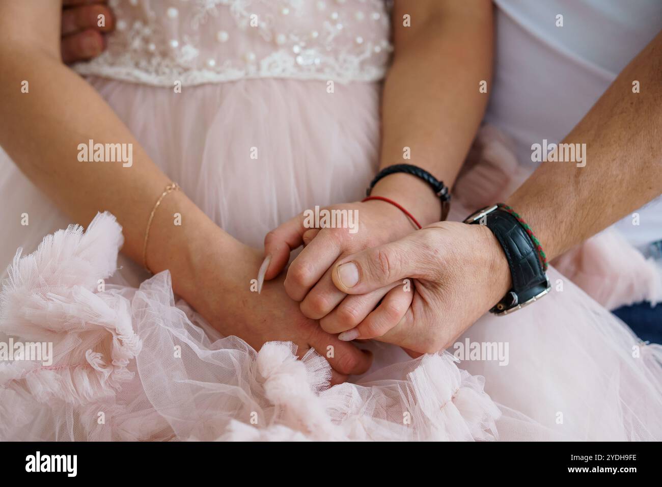 Ein zärtlicher Moment: Ineinander verflochtene Hände aus weichem rosa Stoff. Stockfoto