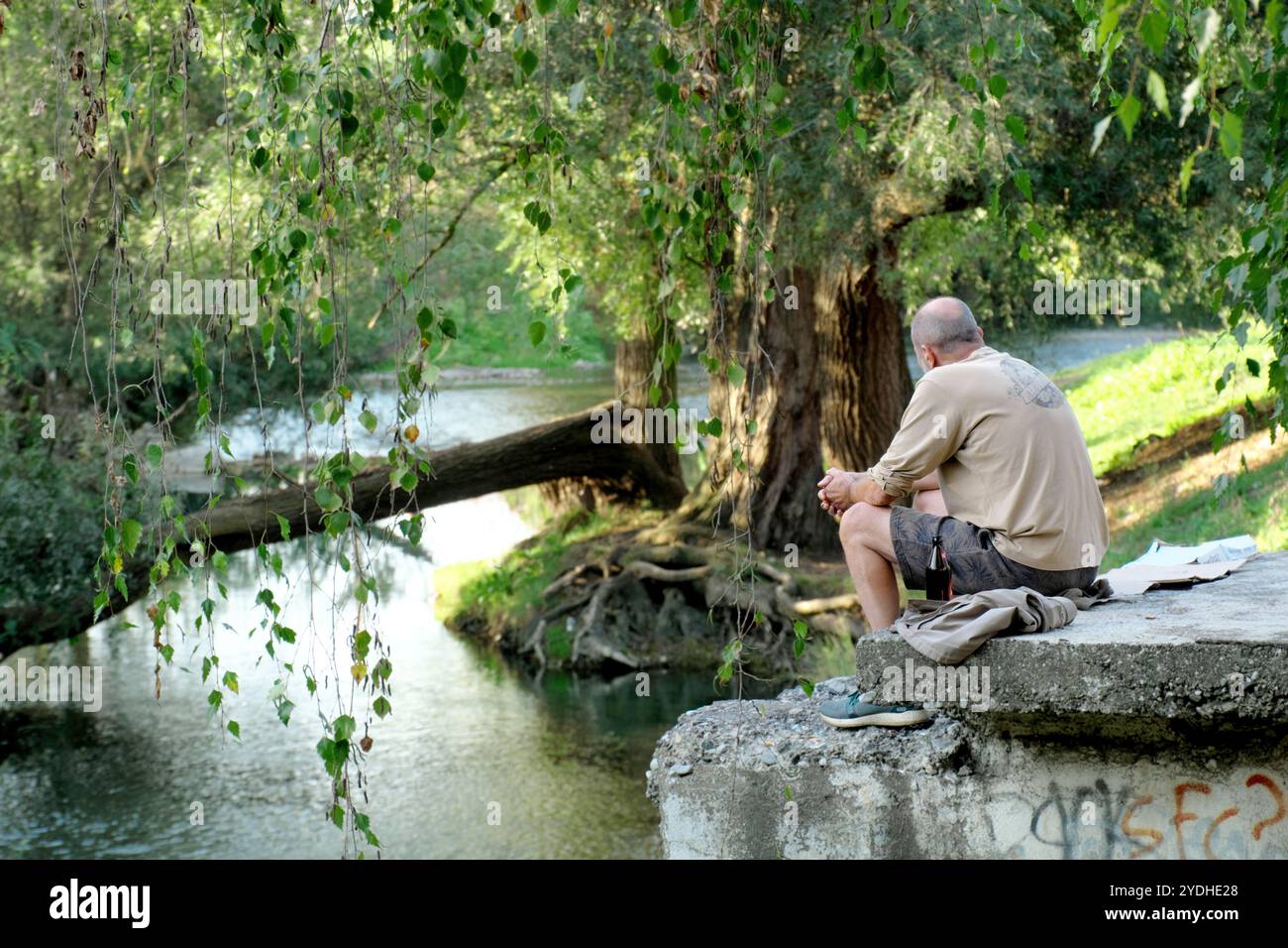 Ein Mann mit einer Flasche Bier entspannt sich am Flussufer in Valjevo, Serbien Stockfoto