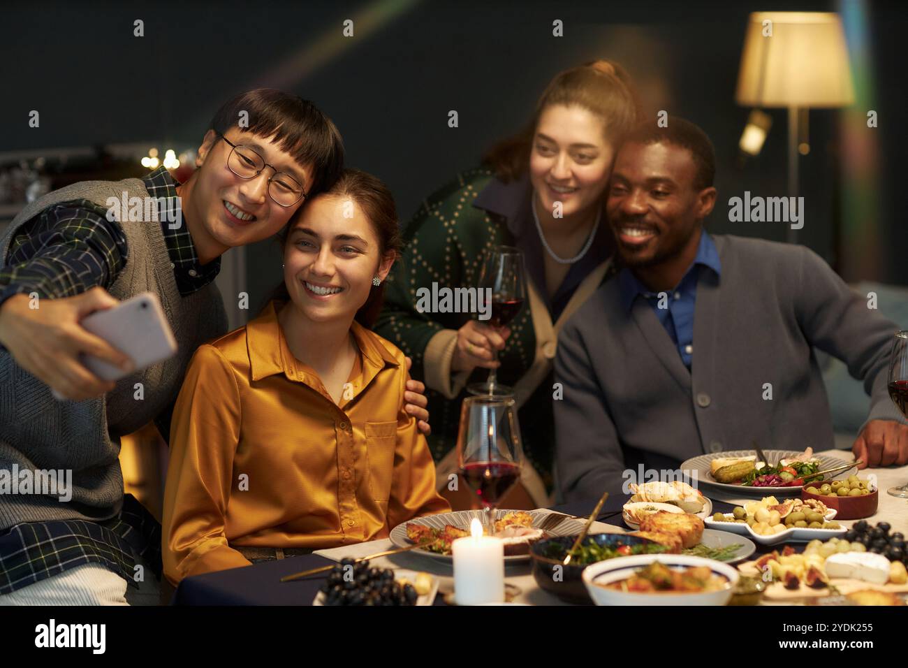 Freimütige Aufnahme eines asiatischen Mannes, der mit vier fröhlichen Freunden Selfie macht, während er am festlichen Esstisch sitzt, Weihnachten zu Hause feiert, Kopierraum Stockfoto