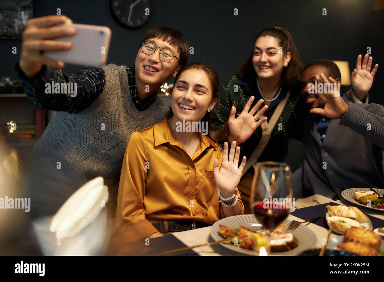 Freimütige Aufnahme eines asiatischen Mannes, der Selfie mit vier fröhlichen Freunden macht, die Hände vor der Kamera winken Stockfoto